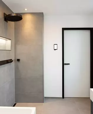 L'illustration montre un aperçu de la salle de bains avec une porte et une poignée de porte R8 ONE en noir graphite.