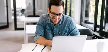 La Photo montre un homme en mode travail devant un ordinateur portable avec un stylo et un bloc.