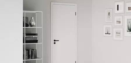 Zu sehen ist ein Wohnraum mit einer weißen Holztür, an welcher der graphitschwarze Türgriff Lucia montiert ist und die passenden graphitschwarzen Bänder.