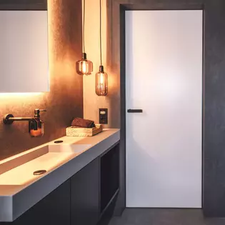La ilustración muestra un cuarto de baño con puerta Vitadoor Modulwerk y Manillas de puerta ONE smart2lock en Negro grafito. 