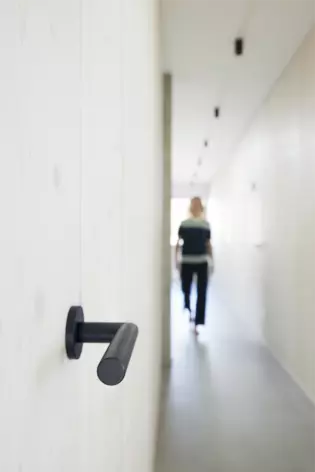 LUCIA smart2lock en Negro grafito Vista lateral La imagen muestra las Manillas de puerta smart2lock Lucia de Griffwerk en Negro grafito desde un lateral. Al fondo, una mujer camina por el pasillo.