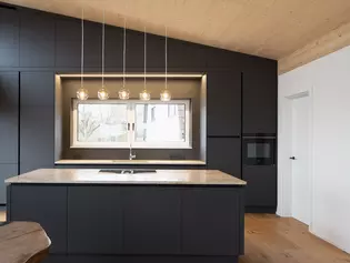 Moderne Küche mit Griffwerk Türgriff TRI Die Abbildung zeigt eine moderne Küche in dunklem grau und Holzakzenten. Die Tür ist mit Griffwerk Türgriff TRI ausgestattet.