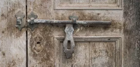 Die Abbildung zeigt eine alte Holztür mit einer rustikalen Metallverriegelung.