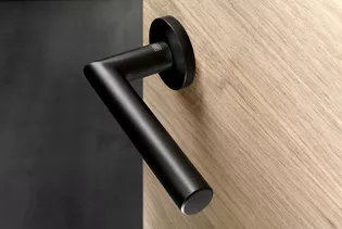 The picture shows the door handle Lucia in graphite black finish mounted on a wooden door.