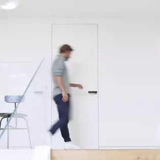  The picture shows a man running to a door and opening it. On the door you can see the Griffwerk door handle R8 One in graphite black.
