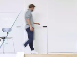 Man walks to the door The picture shows a man running to a door and opening it. On the door you can see the Griffwerk door handle R8 One in graphite black.