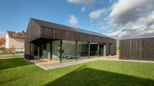 La imagen muestra la casa ana desde el exterior con fachadas de alerce vidriado Negro.