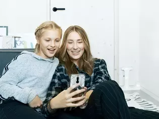 Two children are sitting in the children's room and looking at a cell phone. The door in the background is locked with the help of smart2lock technology and the children have time to themselves, to play and to chat.