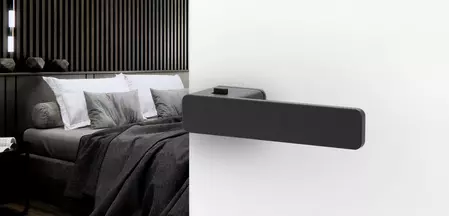 L'illustration montre une porte ouverte avec une poignée de porte R8 ONE smart2lock noire et une chambre à coucher meublée en noir en arrière-plan.