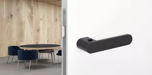 The image shows the Griffwerk door handle AVUS One with a living room.