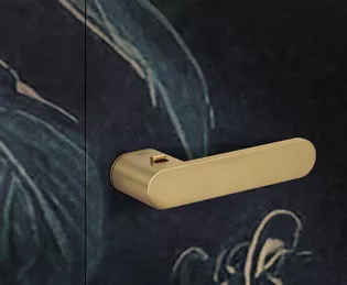 L'illustration montre la poignée de porte ONE en or montée sur une porte à motifs.