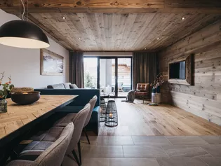  The picture shows the living and dining room with balcony. The premises are finished in simple gray tones with a lot of wood and marble. 