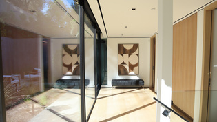 Die Abbildung zeigt einen Vorraum mit Fensterfront und wegführenden Holztüren. 