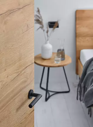 La photo montre une porte en bois ouverte en détail avec les poignées de porte Lucia smart2lock en Noir graphite.