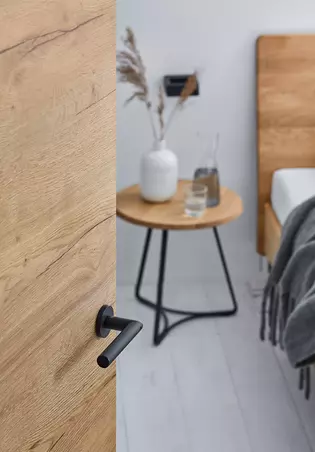 Das Bild zeigt eine geöffnete Holztür im Detail mit Griffwerk Türgriff Lucia smart2lock in Graphitschwarz.