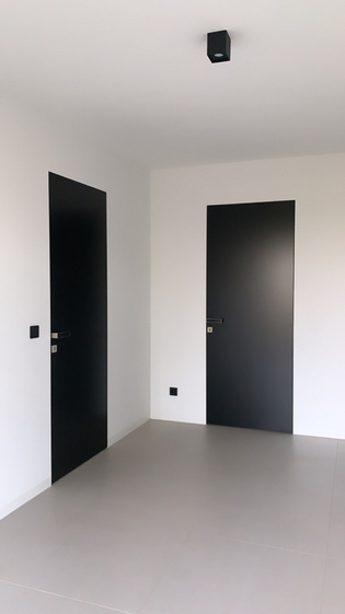 The picture shows a hallway in the Blackhouse with two doors on which the door handle FRAME by Griffwerk in velvety gray is attached.