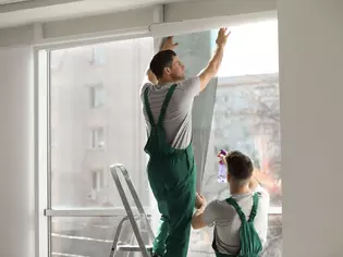 The picture shows two craftsmen darkening a window with foil.