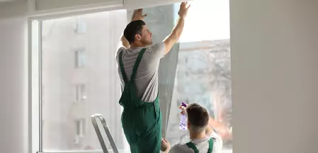 The picture shows two craftsmen darkening a window with foil.