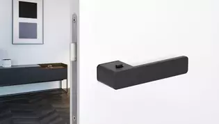 The image shows the Griffwerk door handle R8 One with a living room.