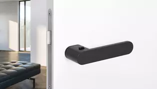 The picture shows the Avus One door handle by Griffwerk in black and a modern room in the background.