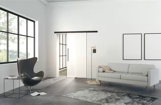 Illustration Planeo Air de Griffwerk Porte coulissante dans le salon L'illustration montre un salon moderne avec la porte coulissante en verre Planeo AIR de Griffwerk sur un mur.