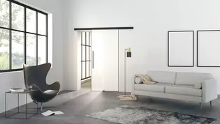 Illustration Planeo Air de Griffwerk Porte coulissante dans le salon L'illustration montre un salon moderne avec la porte coulissante en verre Planeo AIR de Griffwerk sur un mur.
