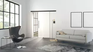 Illustration Planeo Air de Griffwerk Porte coulissante dans le salon L'illustration montre un salon moderne avec la porte coulissante en verre Planeo AIR de Griffwerk sur un mur.