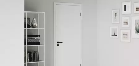 You can see a living room with a white wooden door, on which is mounted graphite black door handle Lucia and matching graphite black hinges.