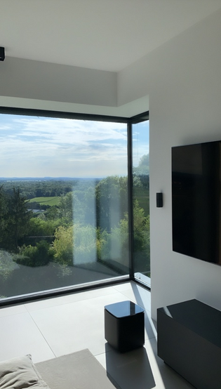 Die Abbildung zeigt das Wohnzimmer im Blackhouse und den Ausblick aus dem Fenster in die Natur.