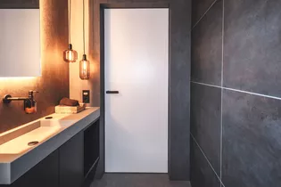 La ilustración muestra un cuarto de baño con puerta Vitadoor Modulwerk y Manillas de puerta ONE smart2lock en Negro grafito. 