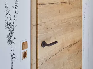 Chambre d'adolescent avec porte en bois et poignées Poignées de porte Lucia smart2lock Noir graphite La photo montre une chambre d'adolescent avec porte en bois et poignée Poignées de porte Lucia avec smart2lock dans la couleur de surface Noir graphite.