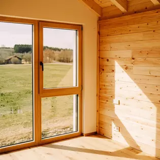 The illustration shows the interior of a wooden house fitted with the AVUS window handle in cashmere grey.