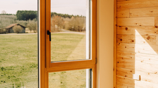 The illustration shows the interior of a wooden house fitted with the AVUS window handle in cashmere grey.