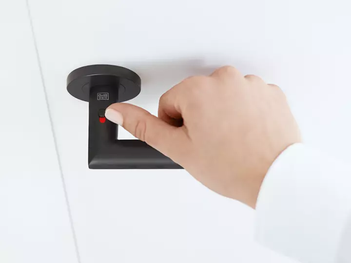 Die Abbildung zeigt den Griffwerk Türgriff Lucia smart2lock in Graphitschwarz mit einer Hand am Griff. Die Hand verschließt den Türgriff am Verriegler.