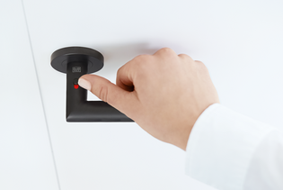 La ilustración muestra las Manillas de puerta smart2lock Lucia de Griffwerk en Negro grafito con una mano en la manilla. La mano cierra la Manillas de puerta en el pestillo.
